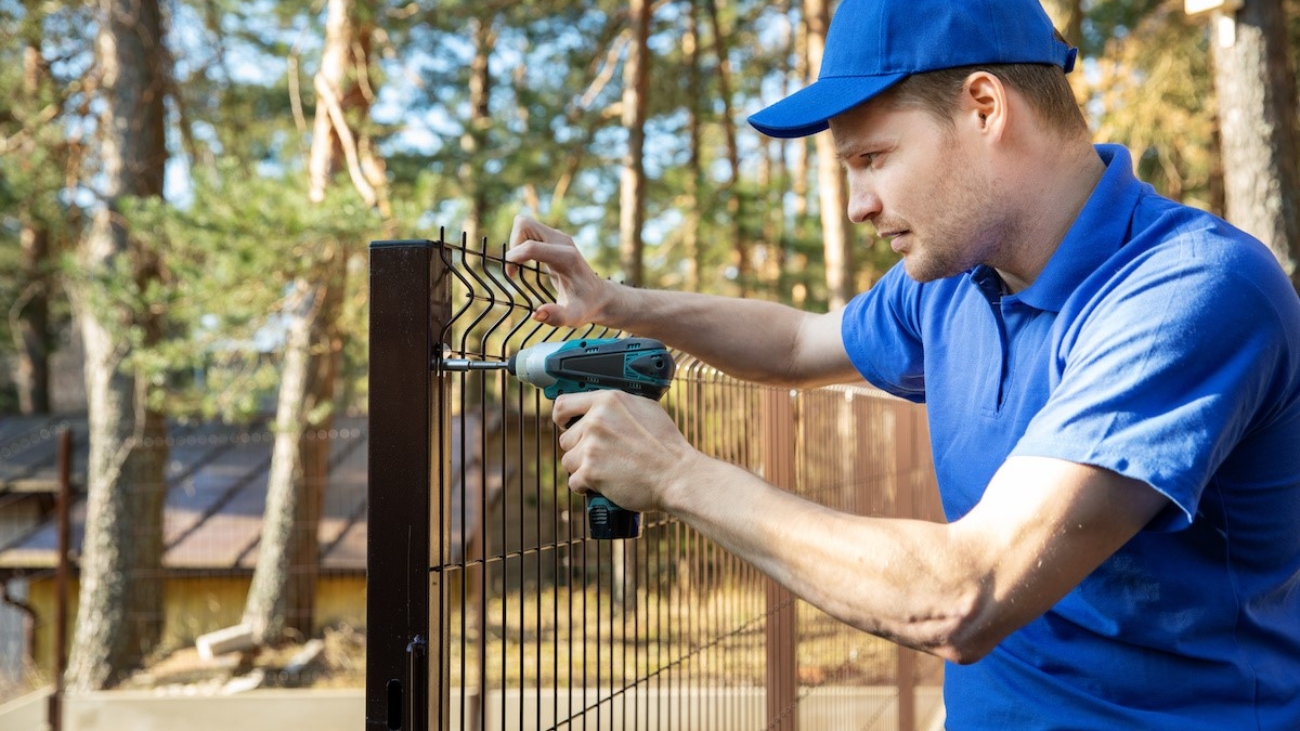fencing services - worker installing welded metal mesh fence